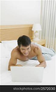 High angle view of a mid adult man lying on the bed using a laptop