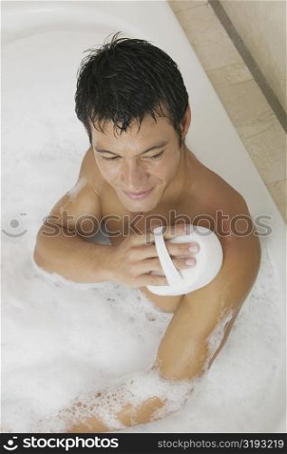 High angle view of a mid adult man scrubbing his body with a loofah in a bathtub