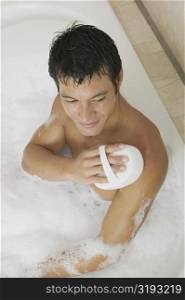High angle view of a mid adult man scrubbing his body with a loofah in a bathtub