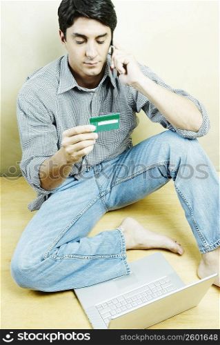High angle view of a mid adult man talking on a mobile phone and holding a credit card
