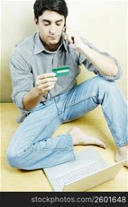 High angle view of a mid adult man talking on a mobile phone and holding a credit card