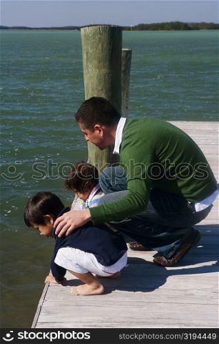 High angle view of a mid adult man with his son and daughter crouching on a pier and looking into the water
