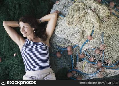High angle view of a mid adult woman lying on commercial fishing nets and smiling