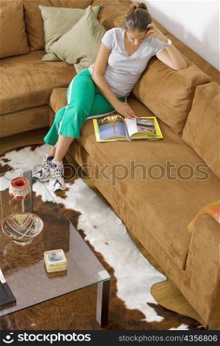 High angle view of a mid adult woman sitting on a couch and reading a book