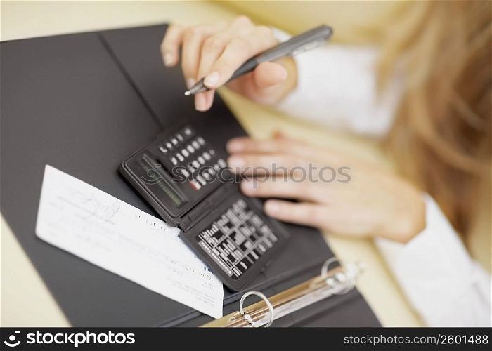 High angle view of a person using a calculator and holding a pen
