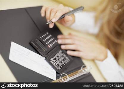 High angle view of a person using a calculator and holding a pen