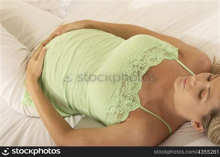 High angle view of a pregnant woman lying on the bed with her hands on her abdomen