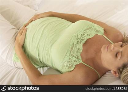 High angle view of a pregnant woman lying on the bed with her hands on her abdomen