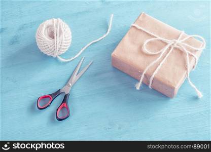 High angle view of a self-made gift box with the twine and the scissors near it, on a blue wooden table