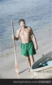 High angle view of a senior man holding an oar on the beach