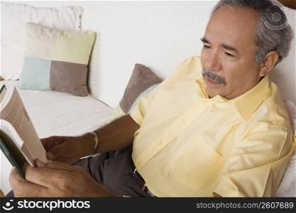 High angle view of a senior man sitting on a couch and holding a book