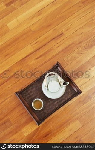 High angle view of a teapot and a tea cup with a tray on a hardwood floor