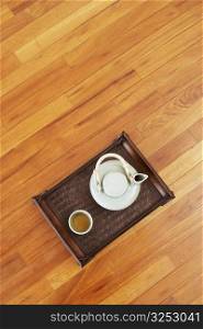 High angle view of a teapot and a tea cup with a tray on a hardwood floor