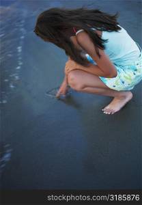 High angle view of a teenage girl drawing in the sand with her finger