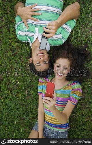 High angle view of a young couple lying in a park and holding mobile phones