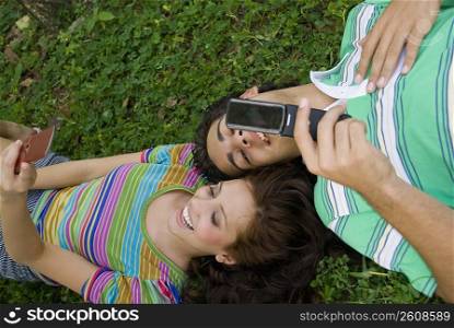 High angle view of a young couple lying in a park and holding mobile phones