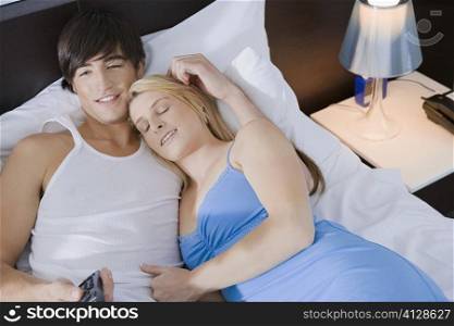 High angle view of a young couple lying on the bed and watching television
