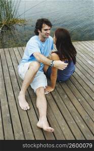 High angle view of a young couple sitting at a pier and looking at each other