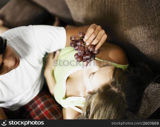 High angle view of a young man feeding a young woman red grapes
