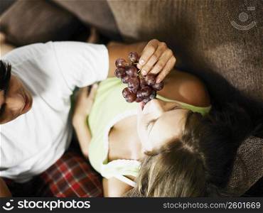 High angle view of a young man feeding a young woman red grapes