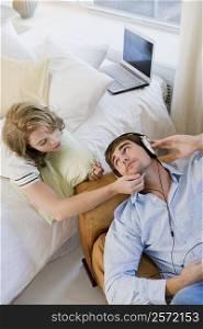 High angle view of a young man listening to music and a young woman lying on the bed beside him