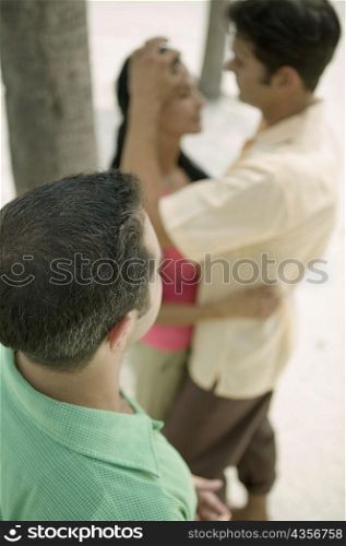 High angle view of a young man looking at a young couple embracing each other