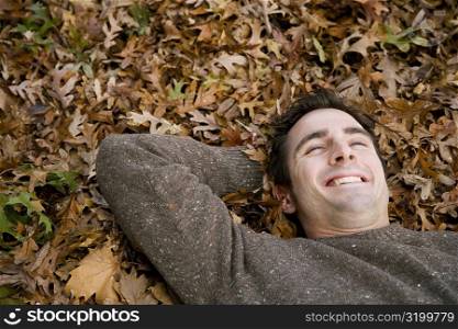 High angle view of a young man lying on leaves and smiling