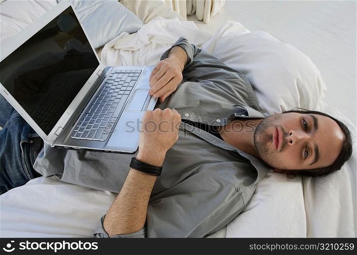 High angle view of a young man lying on the bed and a laptop on his stomach
