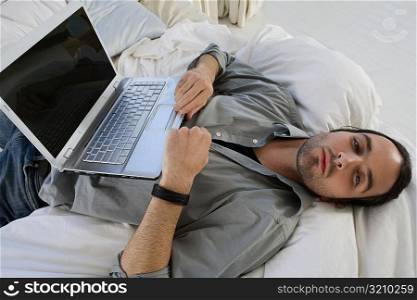 High angle view of a young man lying on the bed and a laptop on his stomach