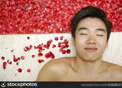 High angle view of a young man lying on the floor near a hot tub filled with rose petals