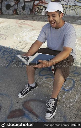 High angle view of a young man reading a book and laughing