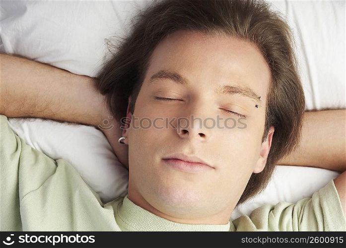 High angle view of a young man sleeping with his hands behind his head