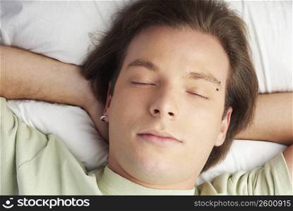 High angle view of a young man sleeping with his hands behind his head