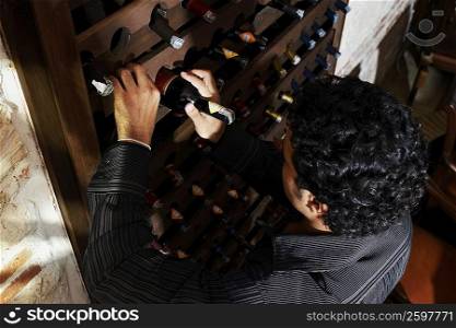 High angle view of a young man taking a bottle from a wine rack