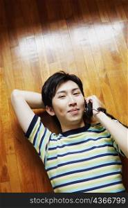 High angle view of a young man talking on the telephone and lying on a hardwood floor