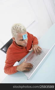 High angle view of a young man using a laptop with an adhesive note on his forehead