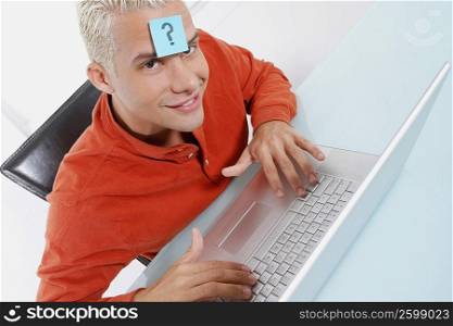 High angle view of a young man using a laptop with an adhesive note on his forehead