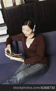 High angle view of a young woman holding a CD case listening to music with headphones