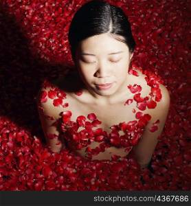 High angle view of a young woman in a bath tub full of rose petals with her eyes closed