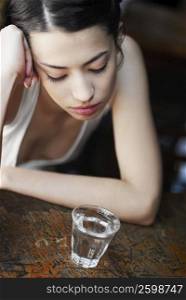 High angle view of a young woman looking at a glass of water and thinking