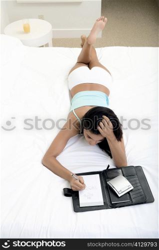 High angle view of a young woman lying on a bed and writing in a personal organizer