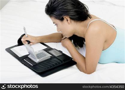 High angle view of a young woman lying on a bed and writing in a personal organizer