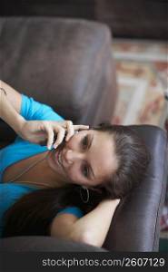 High angle view of a young woman lying on a couch and talking on a mobile phone