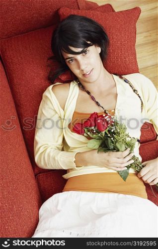 High angle view of a young woman lying on a couch and holding a bunch of flowers