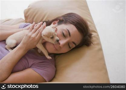 High angle view of a young woman lying on a couch and hugging a puppy