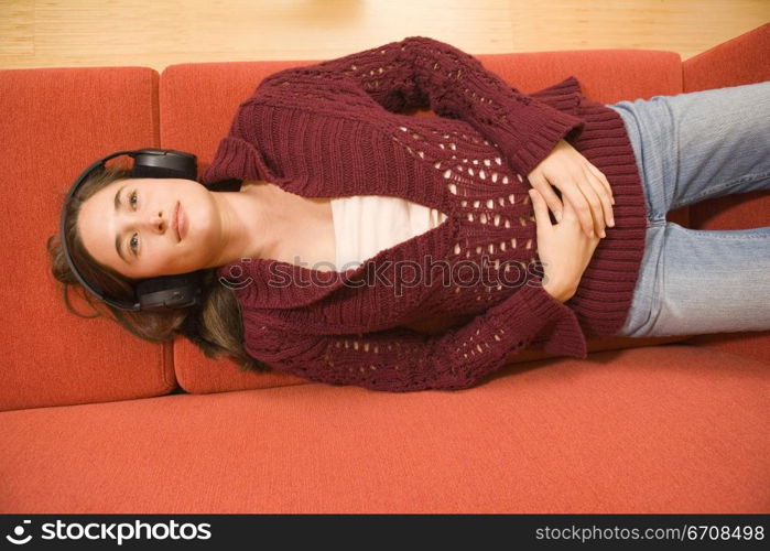 High angle view of a young woman lying on a couch and listening to music