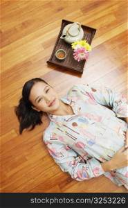 High angle view of a young woman lying on a hardwood floor with a tray beside her