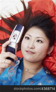 High angle view of a young woman lying on her back holding a mobile phone