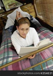 High angle view of a young woman lying on the bed and reading a book