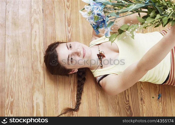 High angle view of a young woman lying on the floor and holding up a bunch of flowers